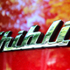 A close up photo of the Ghibli badge on a red Maserati.